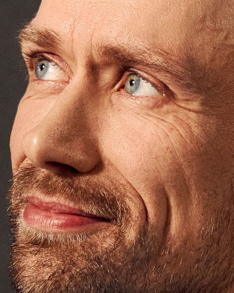 Mand med rødt skæg og blå øjne ser direkte mod kameraet mod mørk baggrund