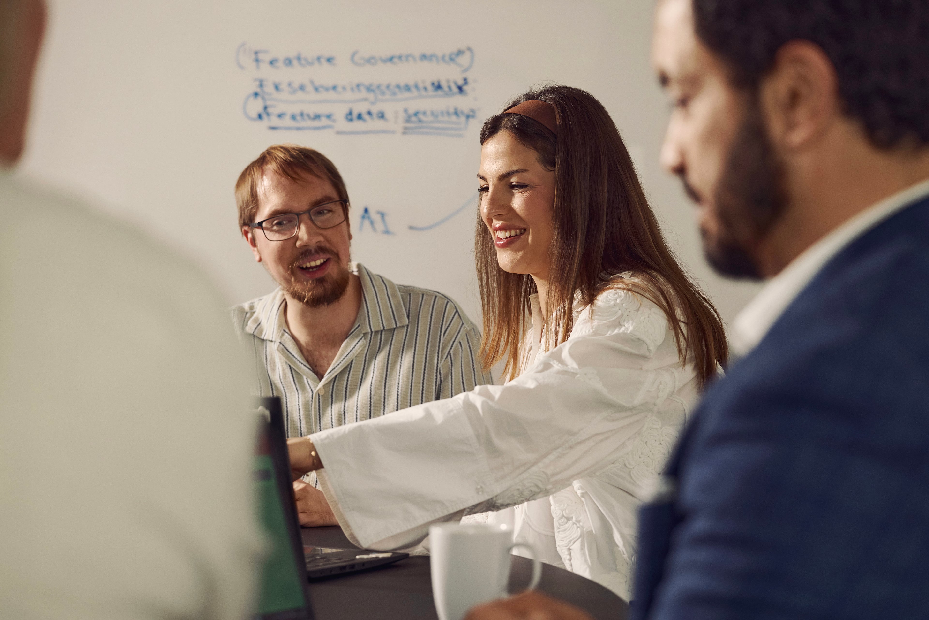 Arbejdsgruppe diskuterer dokumenter ved whiteboard med notater om feature governance og data.